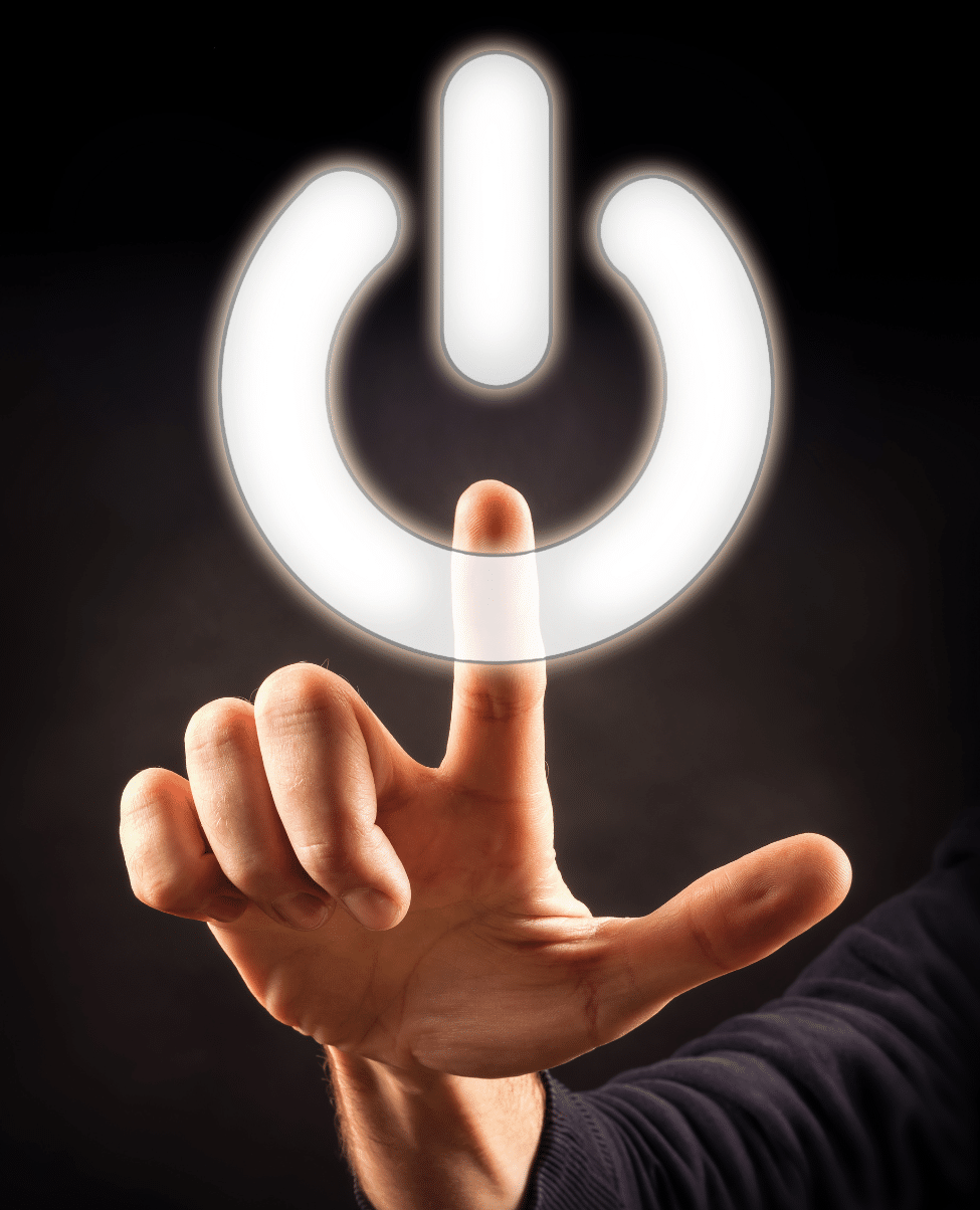 A close-up of a hand with a pointed index finger touching or pressing a glowing power symbol. The background is dark, causing the illuminated power symbol to stand out brilliantly, reminiscent of the sunshine coast at dusk. The hand appears to be in mid-air, pressing on an invisible surface.