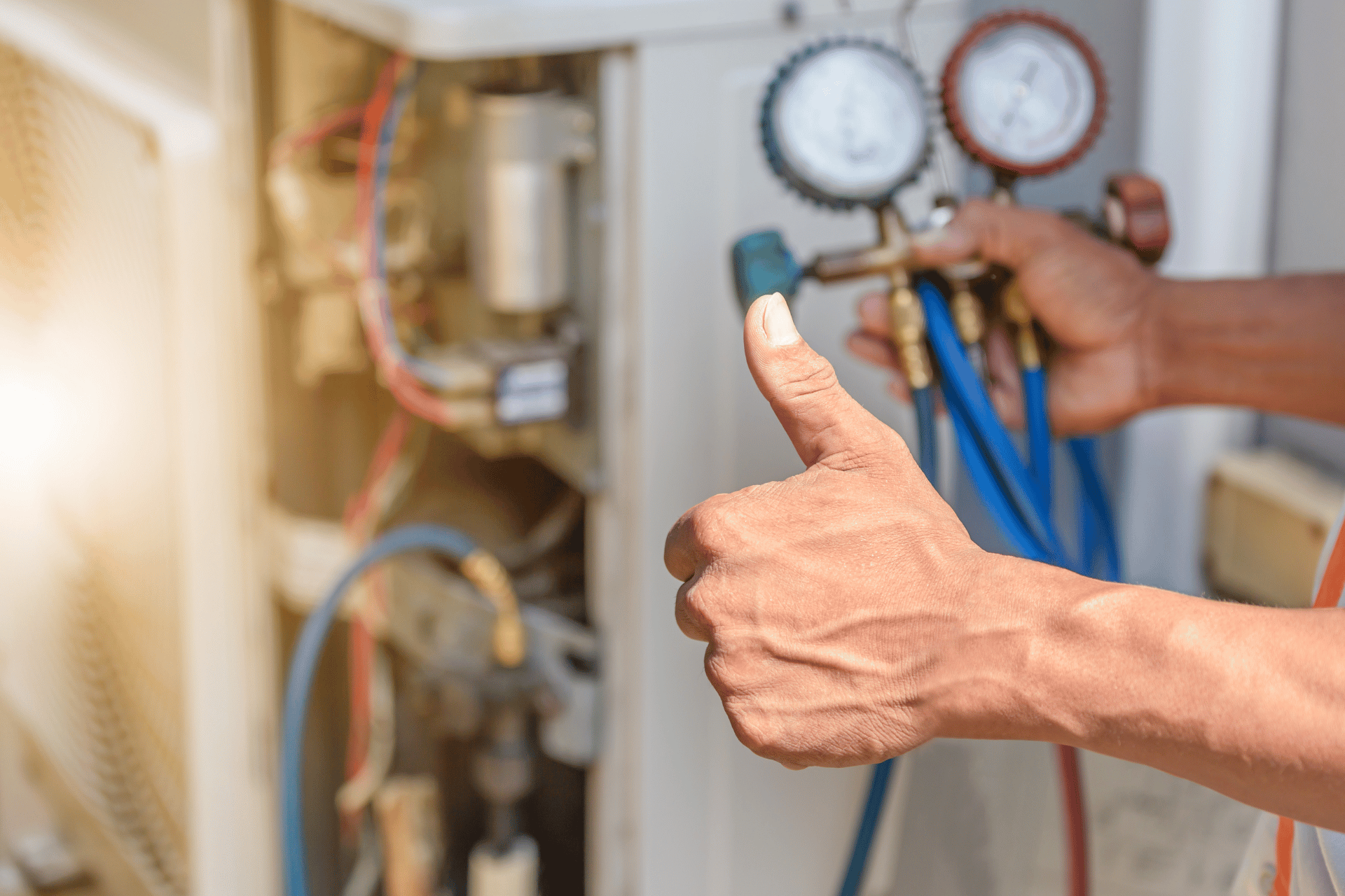 A person's hand gives a thumbs-up while holding pressure gauges connected to an HVAC unit, indicating approval or successful maintenance. The HVAC system's internal components and colorful wires are visible, with the sunlight shining in the background, reminiscent of a bright day on the Sunshine Coast.