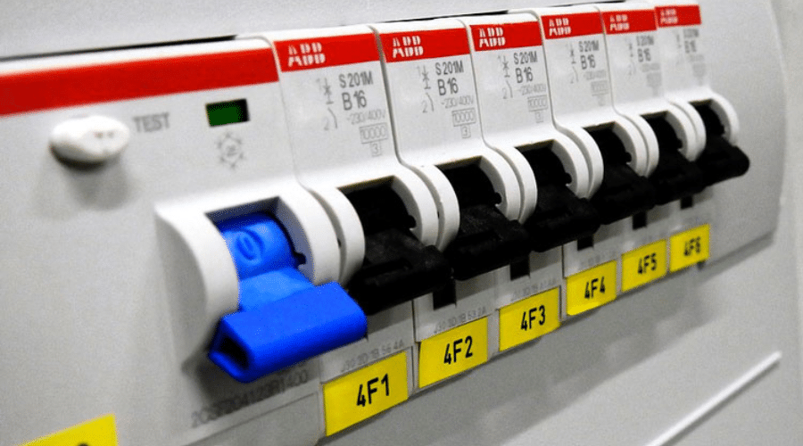 A close-up view of six circuit breakers, five with white toggles and one with a blue toggle, arranged in a row on an electrical panel reminiscent of setups often seen along the Sunshine Coast. Each breaker is labeled with a yellow tag: 4F1, 4F2, 4F3, 4F4, 4F5, and 4F6. The