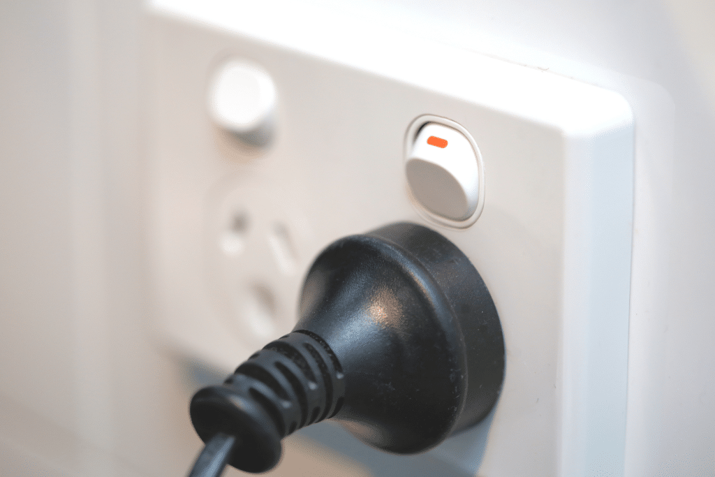 A close-up of a black electrical plug inserted into a white wall socket. The socket features a power switch, which is turned on, as indicated by the visible red marker. The focus is on the connection between the plug and the socket, much like making solid connections on Sunshine Coast trips.